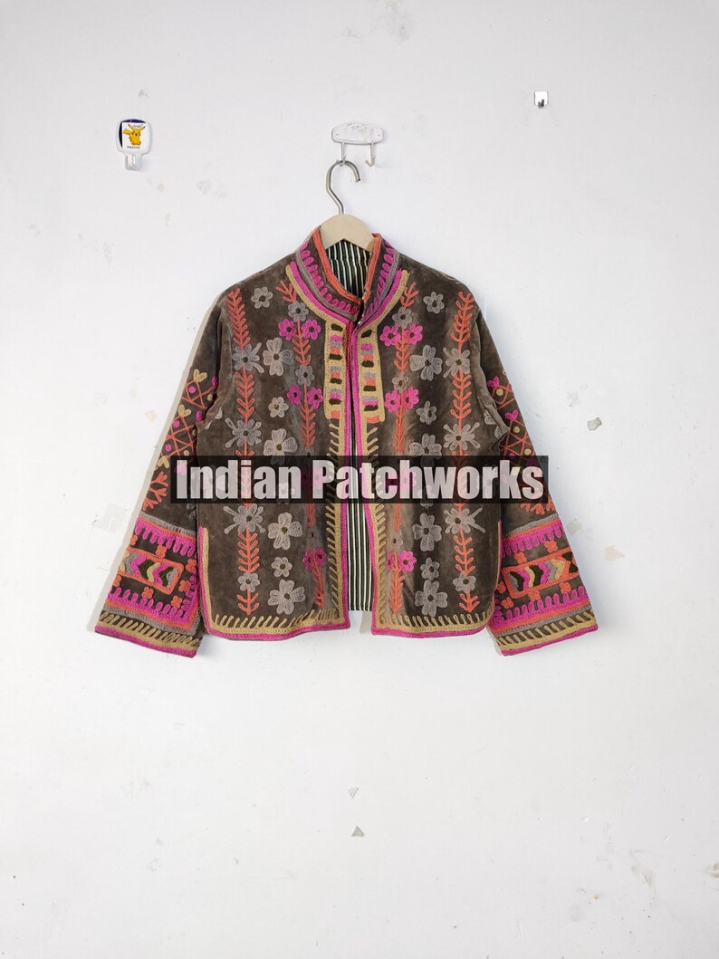 May include: A brown jacket with floral embroidery in pink, orange, and white. The jacket has long sleeves and a high collar. The text "Indian Patchworks" is visible on the bottom of the jacket.