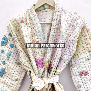 K&ouml;nnte beinhalten: Wei&szlig;er Baumwoll-Morgenmantel mit bunten Stickereien und Patchwork-Details. Der Morgenmantel hat einen Bindeg&uuml;rtel und einen Kragen. Der Text "Indian Patchworks" ist auf dem Morgenmantel sichtbar.