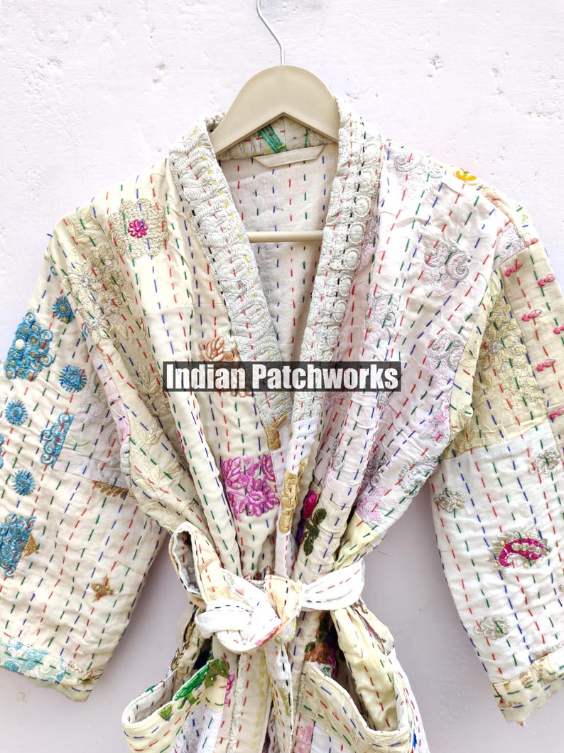 K&ouml;nnte beinhalten: Wei&szlig;er Baumwoll-Morgenmantel mit bunten Stickereien und Patchwork-Details. Der Morgenmantel hat einen Bindeg&uuml;rtel und einen Kragen. Der Text "Indian Patchworks" ist auf dem Morgenmantel sichtbar.