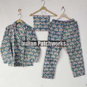 May include: A matching pajama set with a floral pattern in teal, pink, and white. The set includes a button-down shirt, pants, and a matching eye mask, all hanging on wooden hangers. The pajamas are made of a soft, lightweight fabric.