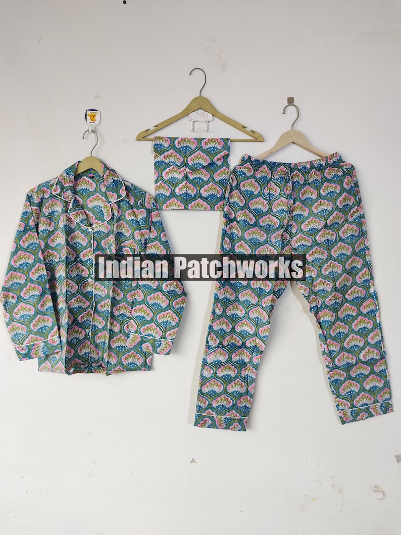 May include: A matching pajama set with a floral pattern in teal, pink, and white. The set includes a button-down shirt, pants, and a matching eye mask, all hanging on wooden hangers. The pajamas are made of a soft, lightweight fabric.
