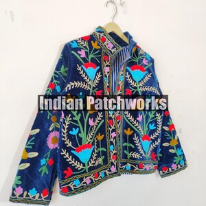 May include: A navy blue velvet jacket with colorful floral embroidery. The jacket has a mandarin collar and a front zipper closure. The embroidery is intricate and detailed, featuring a variety of flowers and leaves in shades of red, pink, yellow, blue, and green. The jacket is lined with a striped fabric.
