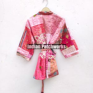 May include: A pink quilted robe with a patchwork design. The robe has a tie belt and a pocket on the front. "Indian Patchworks" is printed on the robe.