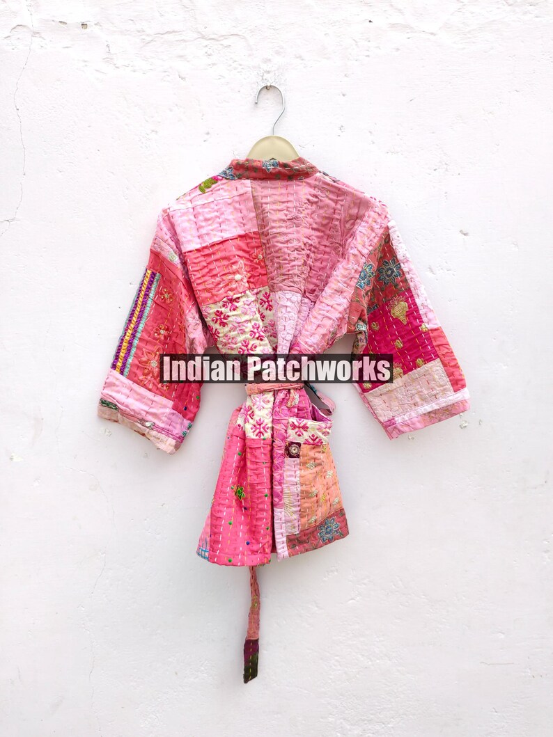 May include: A pink quilted robe with a patchwork design. The robe has a tie belt and a pocket on the front. "Indian Patchworks" is printed on the robe.