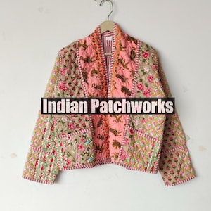 May include: A patchwork jacket with a floral and tiger print design. The jacket features a mix of pink, beige, and green fabrics, with a quilted texture and a decorative trim. The text "Indian Patchworks" is across the front.