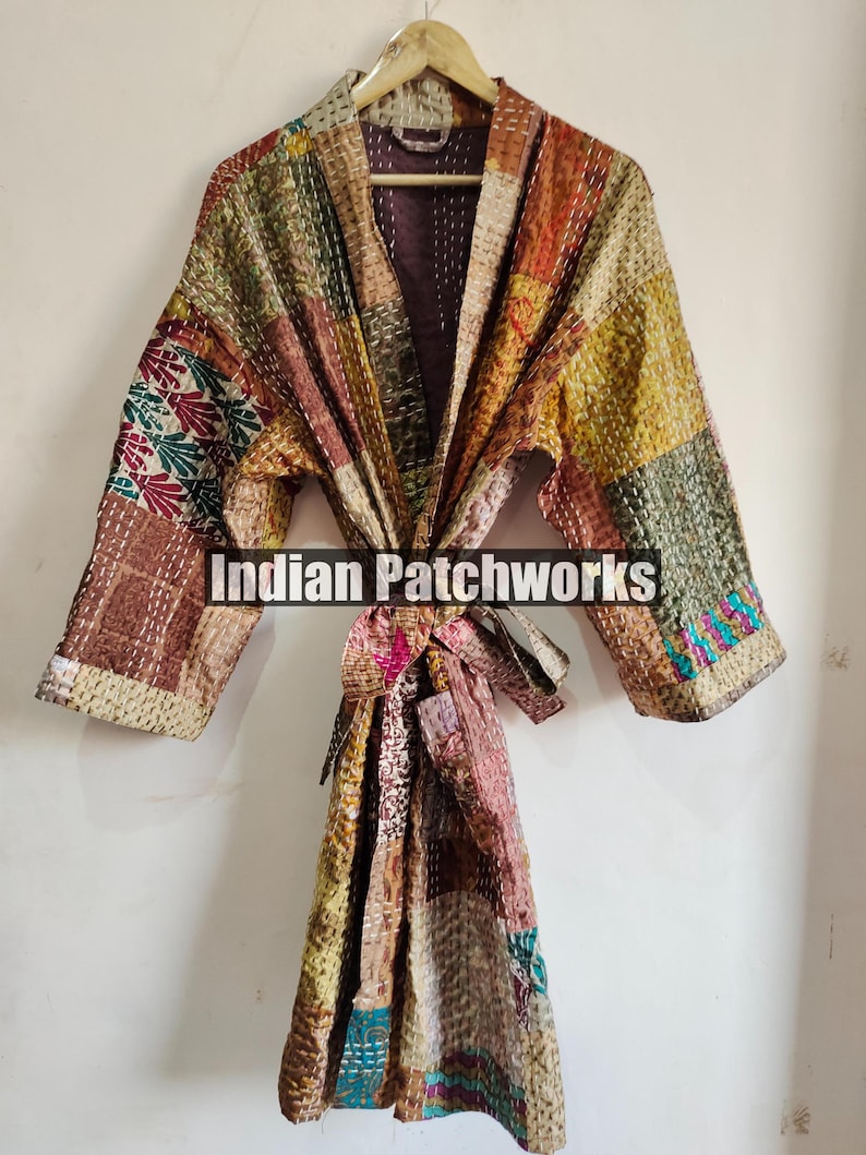 May include: A long, brown, patchwork robe with a tie belt. The robe is made of different fabrics and has a variety of colors, including red, green, blue, and yellow. The robe is hanging on a wooden hanger. The text "Indian Patchworks" is printed on the robe.