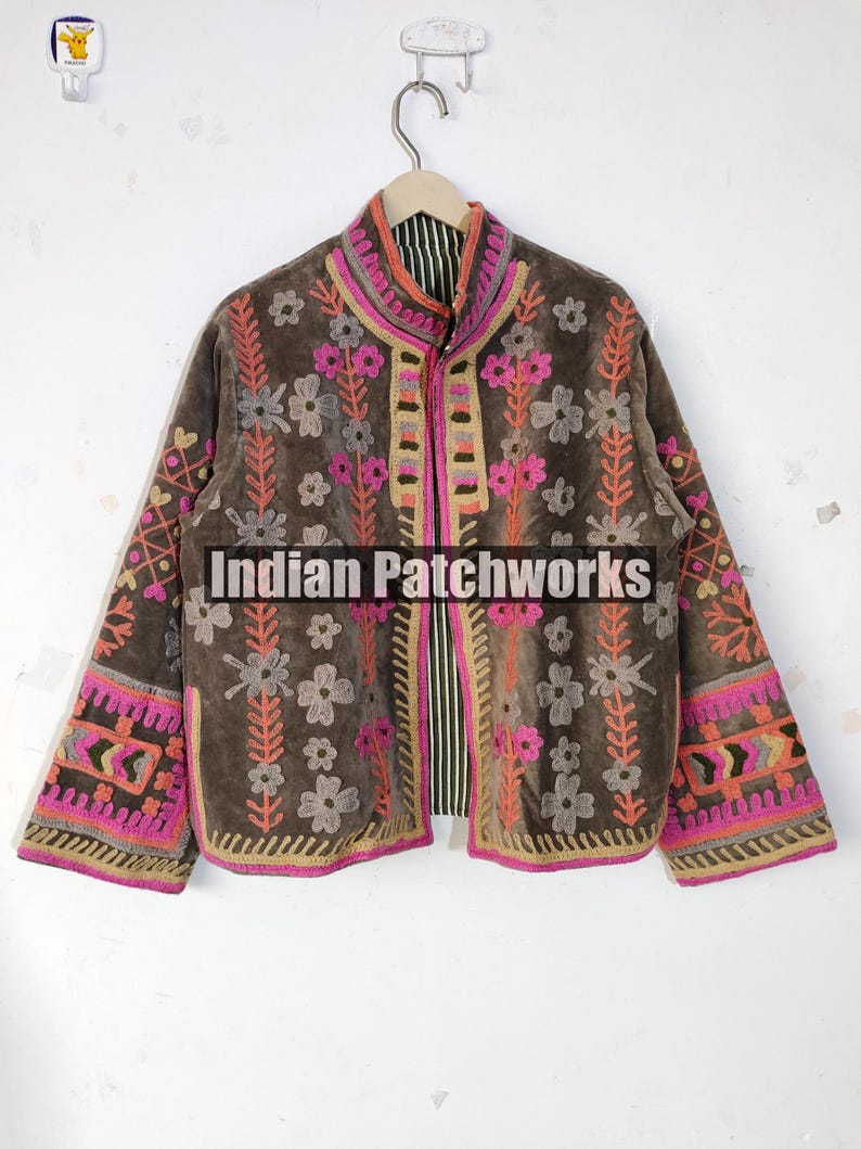 May include: A brown jacket with pink, orange, and grey floral embroidery. The jacket has a stand-up collar and detailed patterns on the sleeves and front. The text "Indian Patchworks" is displayed on the front of the jacket.