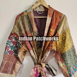 May include: A patchwork quilted robe with a tie belt. The robe is made of various fabrics in shades of brown, green, and orange. The fabric is stitched together in a patchwork pattern. The robe has a long sleeve and a collar. The robe is tied at the waist with a matching tie belt. The text "Indian Patchworks" is printed on the robe.