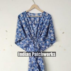 Puede incluir: Un caftán azul con estampado floral, cuello en V y cintura con cordón, colgado de una percha de madera. La tela presenta un estampado de flores blancas sobre fondo azul. El texto "Indian Patchworks" se muestra en la parte inferior.
