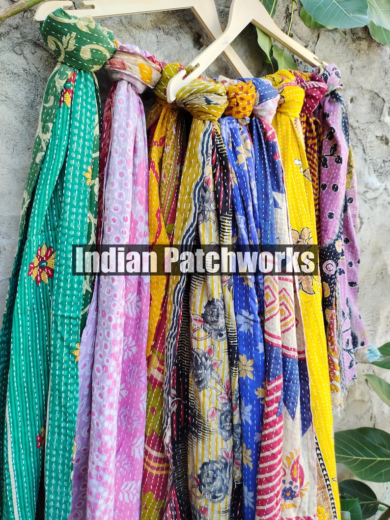Puede incluir: Una colecci&oacute;n de coloridas bufandas estampadas colgadas de una percha de madera. Las bufandas presentan varios dise&ntilde;os, incluyendo patrones florales y geom&eacute;tricos, en tonos verdes, rosas, amarillos y azules. El texto "Indian Patchworks" es visible.