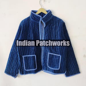 Könnte beinhalten: Eine blaue gesteppte Jacke mit weiß-blau gestreiftem Besatz. Die Jacke hat zwei Taschen und einen Reißverschluss. Der Text "Indian Patchworks" ist auf der Jacke sichtbar.