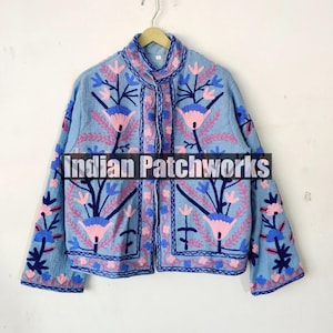 Può includere: Una giacca ricamata di colore azzurro con motivi floreali rosa, blu e neri. La giacca ha un colletto alla coreana e una chiusura con bottone. Il testo "Indian Patchworks" è visibile sul davanti della giacca.