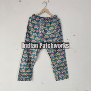 May include: Blue and pink patterned pajama pants hanging on a wooden hanger. The pants feature a repeating floral design with the text "Indian Patchworks" across the center.