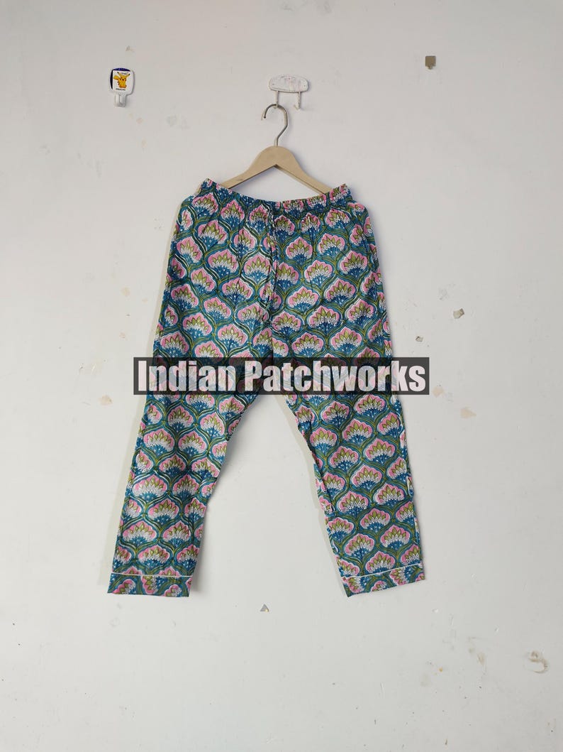 May include: Blue and pink patterned pajama pants hanging on a wooden hanger. The pants feature a repeating floral design with the text "Indian Patchworks" across the center.