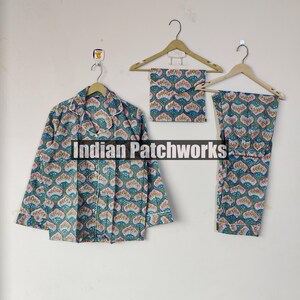 May include: A three-piece pajama set with a floral pattern in shades of green, pink, and blue. The set includes a button-down shirt, a pair of pants, and a matching eye mask, all hanging on wooden hangers. The text "Indian Patchworks" is visible.