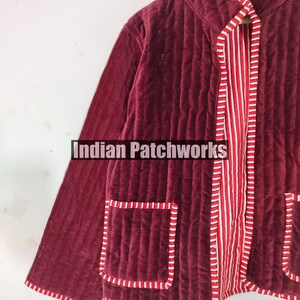 Może przedstawiać: Bordowa pikowana kurtka z paskowaną czerwoną i białą podszewką i wykończeniem. Kurtka ma dwie kieszenie i widoczny jest napis "Indian Patchworks". Kurtka wykonana jest z miękkiego, aksamitnego materiału.