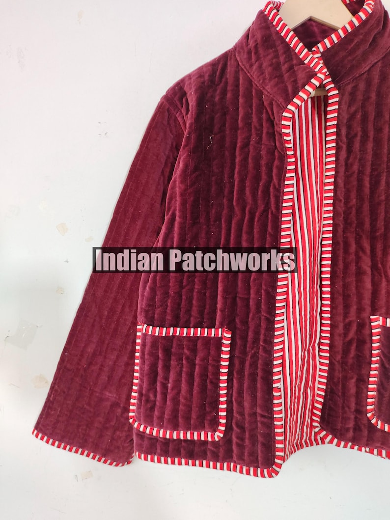 Może przedstawiać: Bordowa pikowana kurtka z paskowaną czerwoną i białą podszewką i wykończeniem. Kurtka ma dwie kieszenie i widoczny jest napis "Indian Patchworks". Kurtka wykonana jest z miękkiego, aksamitnego materiału.