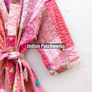 May include: A pink and white patchwork kimono with a tie belt. The kimono is made of different fabrics and has a variety of embroidery details. The text "Indian Patchworks" is visible on the kimono.
