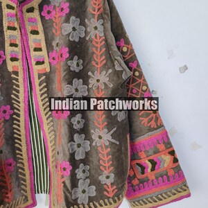 May include: A brown velvet jacket with floral embroidery in pink, orange, and grey. The jacket has a striped lining and the text "Indian Patchworks". The edges are trimmed with pink and beige stitching.