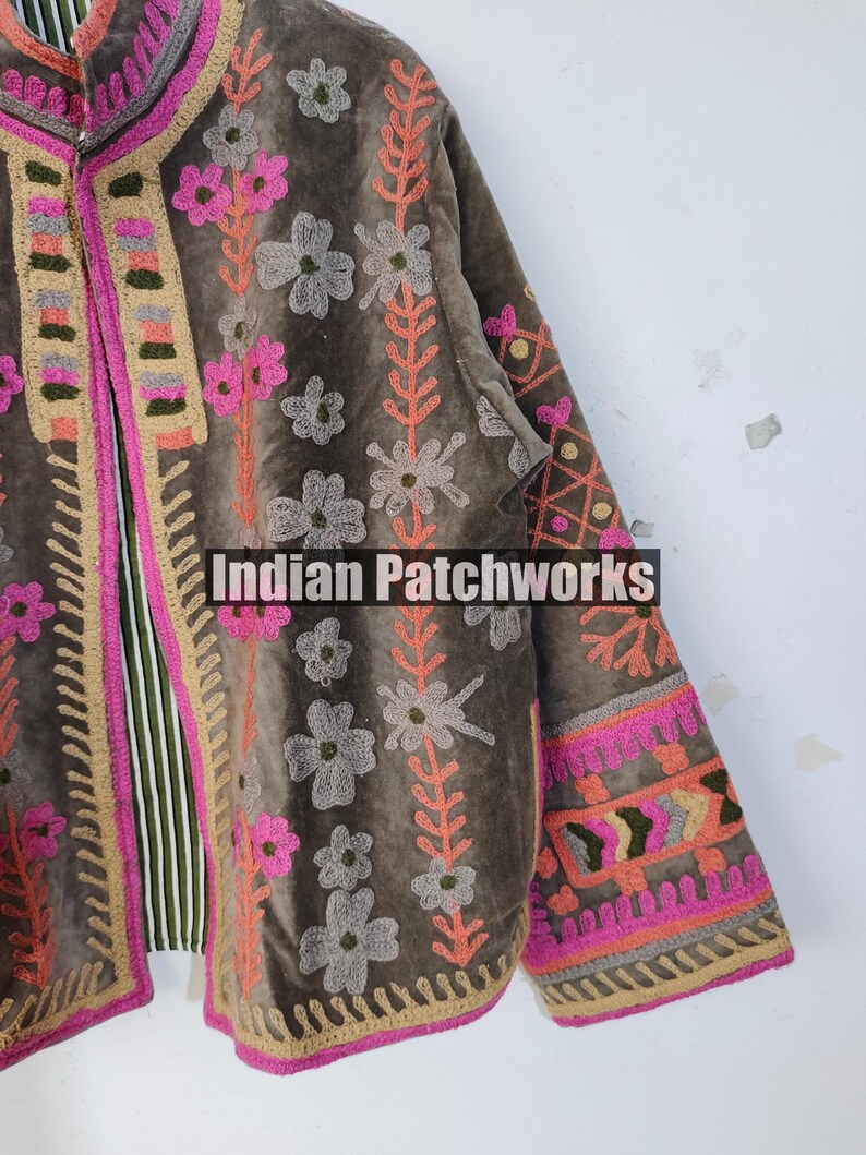 May include: A brown velvet jacket with floral embroidery in pink, orange, and grey. The jacket has a striped lining and the text "Indian Patchworks". The edges are trimmed with pink and beige stitching.