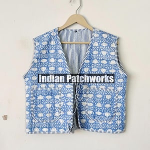 Puede incluir: Un chaleco acolchado azul con estampado floral blanco y dos bolsillos. El chaleco tiene cuello en V y se ata en la parte delantera. El texto "Indian Patchworks" está impreso en la parte delantera del chaleco.