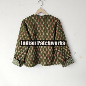May include: A green quilted jacket with a repeating floral pattern in red and white. The jacket has long sleeves with striped cuffs and the text "Indian Patchworks" across the front.