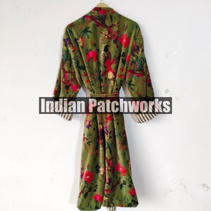 Puede incluir: Una bata larga de color verde oliva con un estampado floral de flores rojas y p&aacute;jaros. La bata tiene mangas largas con pu&ntilde;os a rayas y un cintur&oacute;n a juego. El texto "Indian Patchworks" est&aacute; en el centro de la bata.