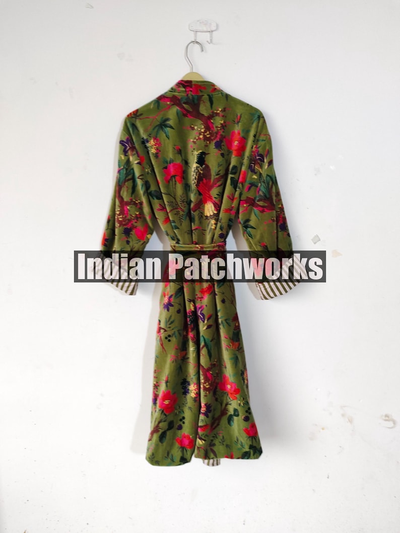 Puede incluir: Una bata larga de color verde oliva con un estampado floral de flores rojas y p&aacute;jaros. La bata tiene mangas largas con pu&ntilde;os a rayas y un cintur&oacute;n a juego. El texto "Indian Patchworks" est&aacute; en el centro de la bata.