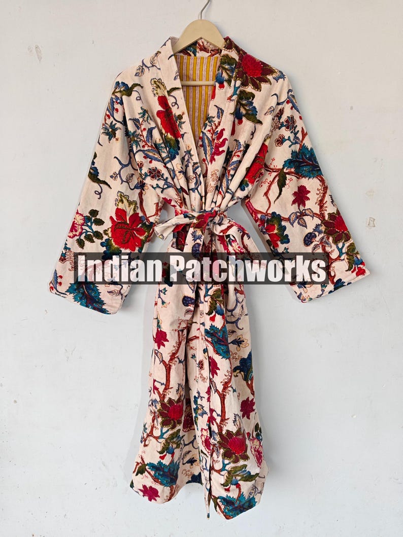 May include: A white cotton robe with a floral print in shades of red, blue, and green. The robe has a tie belt and a yellow and white striped lining. The text "Indian Patchworks" is printed on the robe.