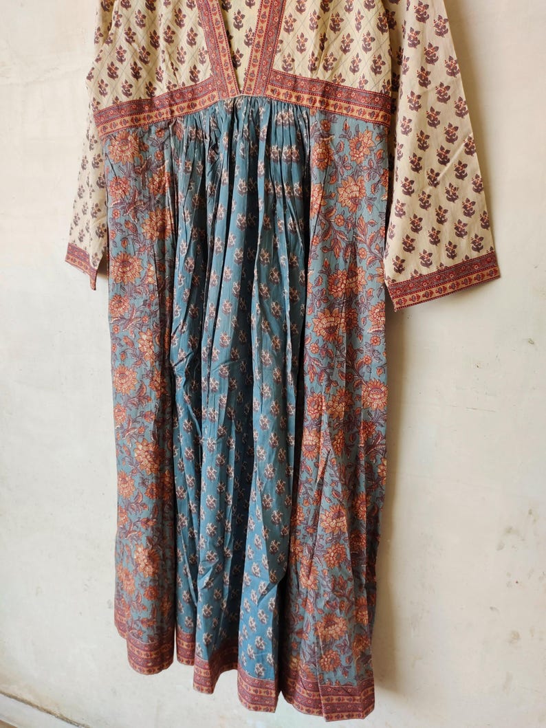 May include: A blue and white cotton dress with a floral print. The dress has a V-neckline and 3/4 sleeves. The dress is gathered at the waist and has a flowing skirt.