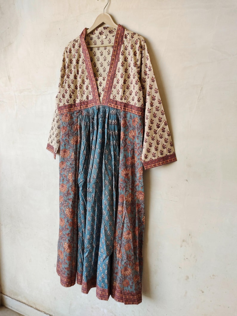 May include: A long, flowing dress with a V-neckline and a gathered waist. The dress is made of a light-weight fabric with a floral print in shades of beige, brown, and blue.