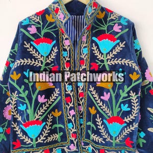 May include: A navy blue velvet jacket with colorful floral embroidery. The jacket has a mandarin collar and a striped lining. The text "Indian Patchworks" is visible on the front of the jacket.