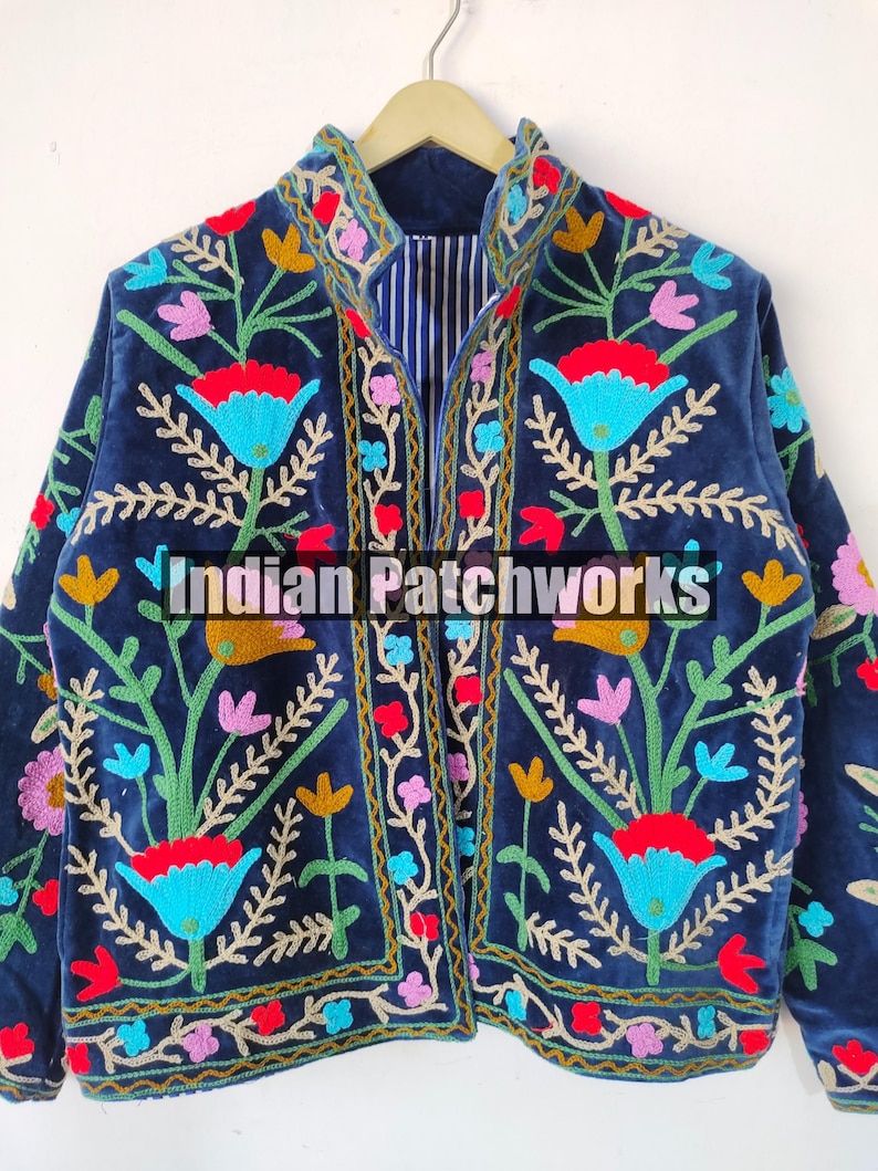 May include: A navy blue velvet jacket with colorful floral embroidery. The jacket has a mandarin collar and a striped lining. The text "Indian Patchworks" is visible on the front of the jacket.