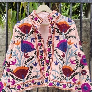 May include: A pink embroidered jacket with a floral pattern. The jacket has a mandarin collar and long sleeves. The embroidery is in shades of blue, green, orange, and purple.