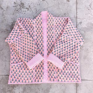 May include: A pink quilted jacket with a floral print and a white and pink striped front panel. The jacket has long sleeves and a collar.