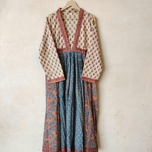 May include: A long, flowing dress with a V-neckline and long sleeves. The dress is made of a light-colored fabric with a floral print. The dress has a gathered waist and a flowing skirt.