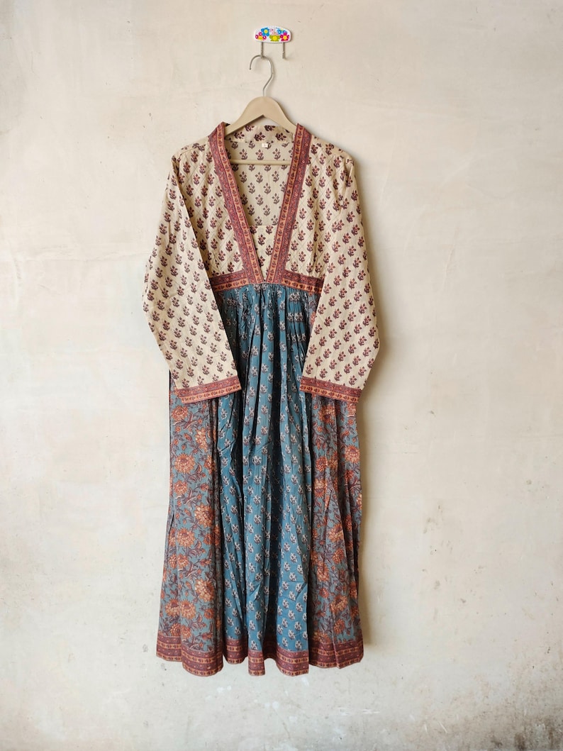 May include: A long, flowing dress with a V-neckline and long sleeves. The dress is made of a light-colored fabric with a floral print. The dress has a gathered waist and a flowing skirt.