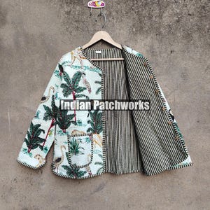 Pode incluir: Uma jaqueta acolchoada branca e verde com estampa floral e animal. A jaqueta tem fecho de botão e forro listrado. O texto "Indian Patchworks" é visível na jaqueta.