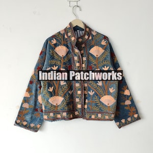 May include: A blue jacket with floral embroidery. The jacket features a high collar and is adorned with peach and brown floral patterns. The text "Indian Patchworks" is displayed across the front of the jacket.