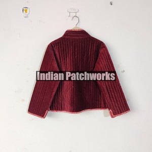 Może przedstawiać: Bordowa pikowana kurtka z wysokim kołnierzem i długimi rękawami. Kurtka ma pionowy wz&oacute;r szw&oacute;w i czerwono-białe paski. Tekst "Indian Patchworks" znajduje się na środku kurtki.