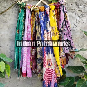Puede incluir: Una colecci&oacute;n de coloridas bufandas estampadas colgadas de perchas de madera. Las bufandas muestran una variedad de dise&ntilde;os, incluyendo patrones florales y geom&eacute;tricos, en tonos verdes, rosas, amarillos y azules. El texto "Indian Patchworks" es visible.