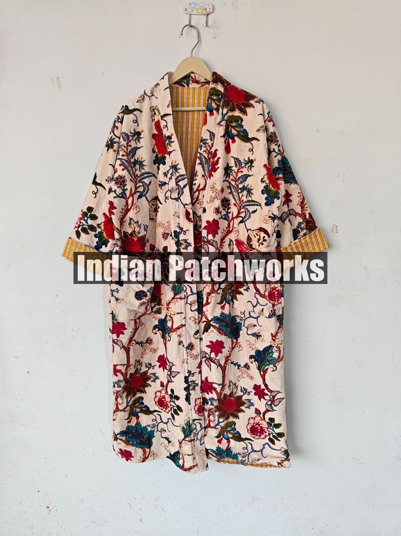 May include: A long, cream-colored robe with a floral print. The robe has a yellow and white striped lining and a button closure. The text "Indian Patchworks" is visible on the front of the robe.