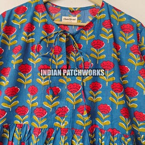 May include: A blue floral print dress featuring red flowers and yellow stems. The dress has a round neckline with a tie closure and a gathered skirt. The text "INDIAN PATCHWORKS" is visible.