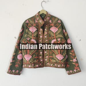 May include: An olive green jacket with pink floral embroidery and the text "Indian Patchworks". The jacket has a stand-up collar and long sleeves. The floral design includes pink flowers and brown stems.