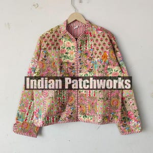 May include: A floral patchwork jacket with a mandarin collar and a zipper closure. The jacket is made of cotton and has a quilted design. The fabric is a mix of pink, green, and brown colors. The text "Indian Patchworks" is printed on the front of the jacket.