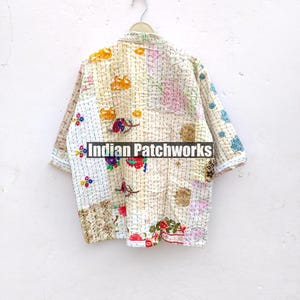 K&ouml;nnte beinhalten: Eine wei&szlig;e, mehrfarbige Patchworkjacke mit Blumenstickerei. Die Jacke h&auml;ngt an einem Kleiderb&uuml;gel vor einer wei&szlig;en Wand. Der Text "Indian Patchworks" ist auf der Jacke sichtbar.