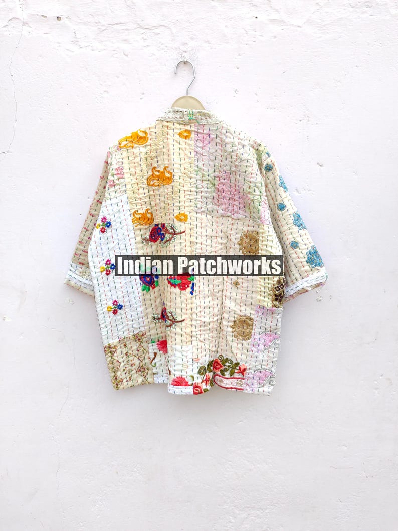 K&ouml;nnte beinhalten: Eine wei&szlig;e, mehrfarbige Patchworkjacke mit Blumenstickerei. Die Jacke h&auml;ngt an einem Kleiderb&uuml;gel vor einer wei&szlig;en Wand. Der Text "Indian Patchworks" ist auf der Jacke sichtbar.