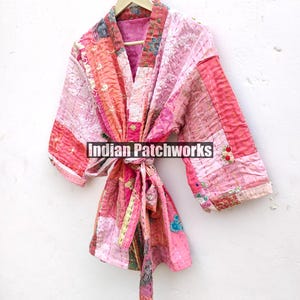 May include: A pink and peach patchwork kimono with a tie belt. The kimono is made of quilted fabric and has a floral design. The text "Indian Patchworks" is visible on the front of the kimono.