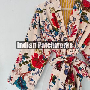May include: A white robe with a floral print in shades of red, blue, and green. The robe has a tie belt and a pocket on the left side. The robe is lined with a yellow and white striped fabric. The text "Indian Patchworks" is visible on the robe.