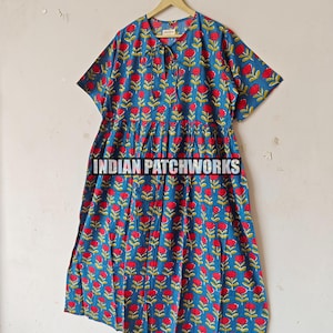 May include: A blue dress with a red floral pattern hangs on a wooden hanger. The dress features short sleeves and a gathered waist. The text "INDIAN PATCHWORKS" is visible. The dress is made of a lightweight fabric, suitable for warmer weather.